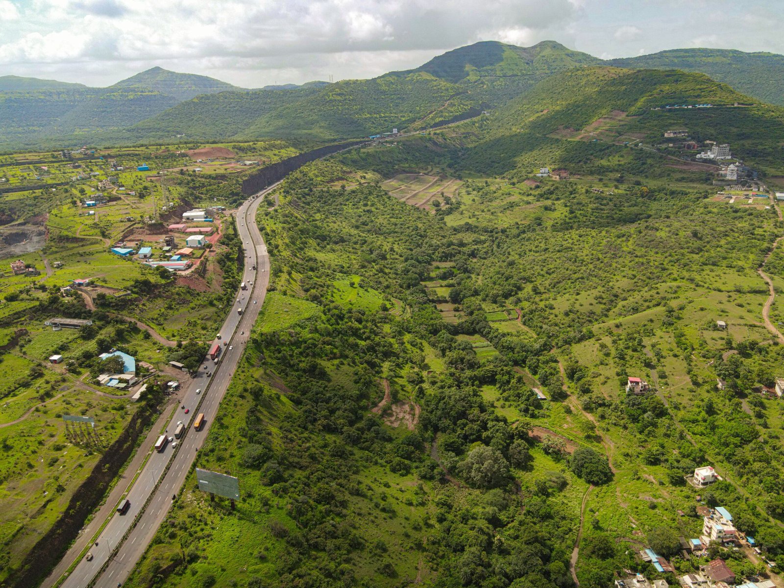 An aerial drone view of Pune Bangalore highway surrounded by green valley and mountains on cloudy day